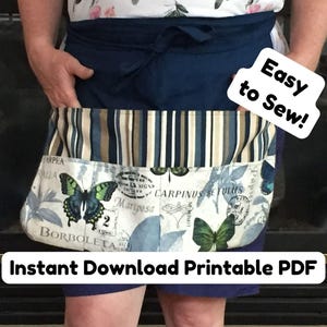 Może przedstawiać: Granatowy fartuch z nadrukiem motyli i botanicznym, z tekstem "Easy to Sew!" i "Instant Download Printable PDF." Fartuch ma kieszeń w paski i wiązany pas.