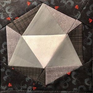 May include: A close-up of a gray and white fabric patchwork design in the shape of a 20-sided die. The fabric is sewn together in a geometric pattern.