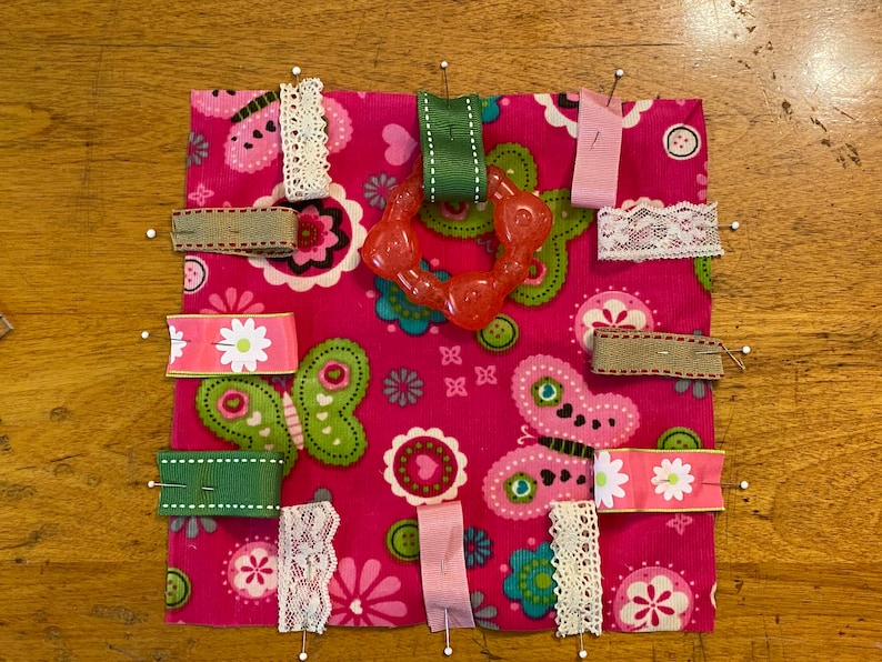 Tags and teething toy pinned to fabric.