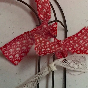 May include: Red and white patterned fabric ribbon tied around a metal wreath form. The ribbon is tied in a bow and the ends are frayed.