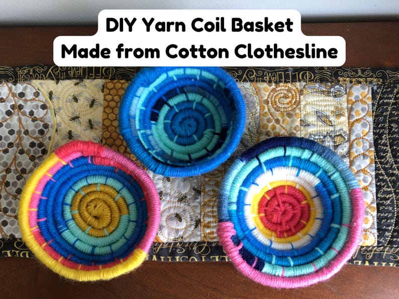 May include: Three round coil baskets made from cotton clothesline wrapped in colorful yarn. One basket features shades of blue, another yellow and pink, and the third pink, blue, and yellow. Text reads: DIY Yarn Coil Basket Made from Cotton Clothesline.