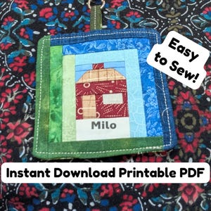 Puede incluir: Un artículo de tela cuadrado hecho a mano con un diseño de casa, el nombre "Milo" y el texto "Easy to Sew!" y "Instant Download Printable PDF". El artículo está hecho de varias piezas de tela coloridas, incluyendo azul, verde y rojo. Tiene un borde verde y un anillo de metal.