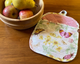 May include: A square fabric potholder featuring a print of yellow flowers and colorful butterflies on a light background. The top section has a textured pink pocket, and a small fabric loop is attached to the top edge for hanging.