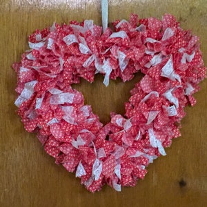 May include: A red and white heart-shaped wreath made of fabric and lace. The wreath is decorated with small white polka dots.