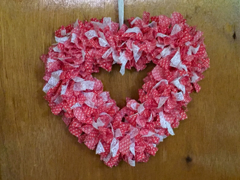 May include: A red and white heart-shaped wreath made of fabric and lace. The wreath is decorated with small white polka dots.
