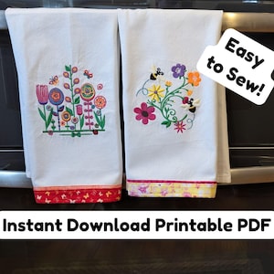 Op de afbeelding: Twee witte keukendoeken met geborduurde bloemenmotieven. De handdoek links heeft een kleurrijk bloemenmotief in rood, oranje, geel, groen, blauw en paars. De handdoek rechts heeft een bloemenmotief in geel, oranje, rood, groen en paars. De handdoeken hangen aan een zwarte ovendeur. Een witte sticker met de tekst "Eenvoudig te naaien!" is bevestigd aan de ovendeur.