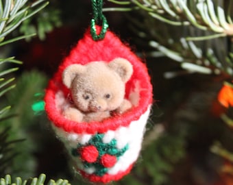 May include: A red and white knitted stocking ornament with a brown teddy bear inside. The stocking has a green holly design with red berries.