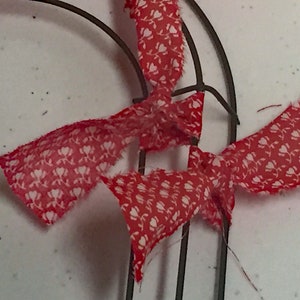 May include: Red and white fabric ribbon tied around a metal wreath form. The ribbon has a small white floral pattern.