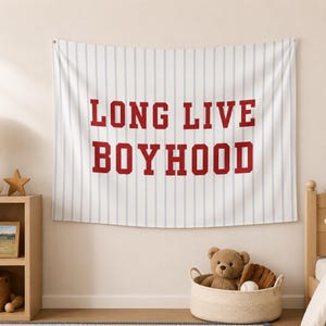 May include: A rectangular wall tapestry featuring a white background with vertical light blue pinstripes. The text LONG LIVE BOYHOOD is printed in large, bold, red block letters across the center of the fabric in a classic athletic style.
