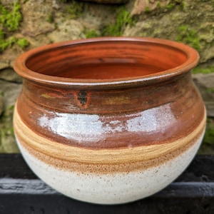 May include: A white ceramic pot with brown and orange glaze. The pot has a rounded shape and a wide opening.