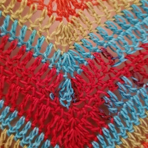 May include: Close-up of a crocheted fabric with a rainbow pattern of orange, yellow, blue, and red.