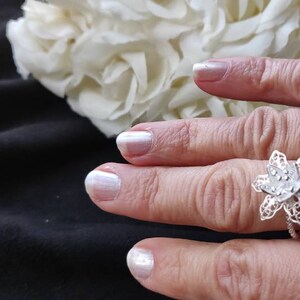 Pode incluir: Um anel de filigrana de prata com um design de flor. O anel est&aacute; em um dedo com esmalte de unha branco.