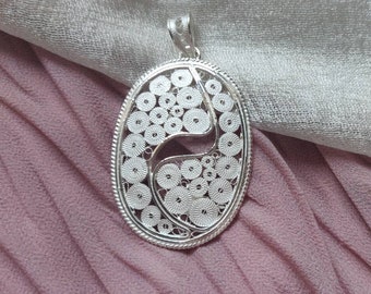 Può includere: Un ciondolo in filigrana d'argento con un designo circolare. Il ciondolo è di forma ovale e presenta un motivo delicato e intricato.