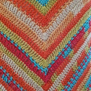 May include: Close-up of a colorful crocheted fabric with a diamond pattern in shades of orange, red, green, blue, and white.