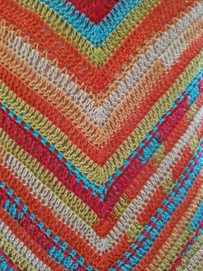 May include: Close-up of a colorful crocheted fabric with a diamond pattern in shades of orange, red, green, blue, and white.