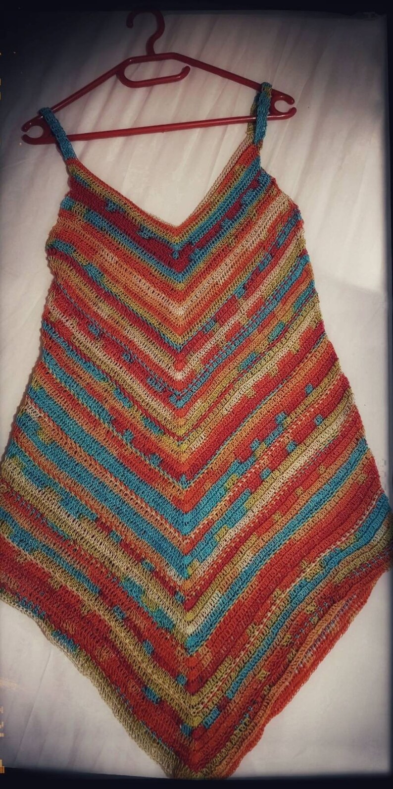 May include: A crocheted top with a V-neck and thin straps. The top is made with a multi-colored yarn in shades of orange, blue, green, and beige. The top is crocheted in a striped pattern.