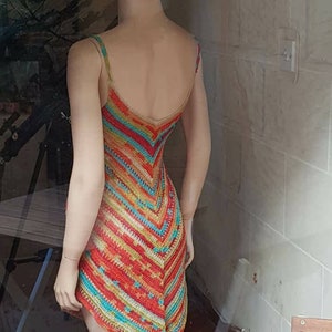 May include: A colorful crochet dress with a geometric pattern in shades of red, orange, yellow, green, and blue. The dress is sleeveless and has a V-neckline.