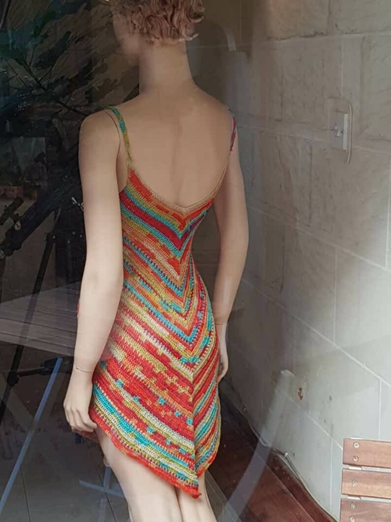 May include: A colorful crochet dress with a geometric pattern in shades of red, orange, yellow, green, and blue. The dress is sleeveless and has a V-neckline.