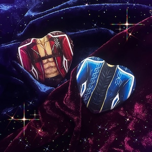 May include: Two heart-shaped artworks showing jackets. One is red with white details, the other is blue with gold and white accents. They are on a velvet surface with a starry background.