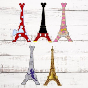 Könnte beinhalten: Fünf Pins im Eiffel-Turm-Design mit verschiedenen Designs. Die Pins sind rot mit weißen Punkten, schwarz mit Mickey-Maus-Ohren, pink mit einem Streifenmuster, grau mit einer Fee und goldfarben.