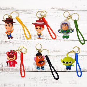 May include: Seven colourful keychains featuring characters from the Toy Story franchise. The characters include Woody, Buzz Lightyear, Jessie, Mr. Potato Head, and Alien. Each keychain has a different coloured strap.