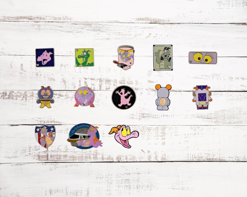 Op de afbeelding: Een verzameling van 13 Disney-pins met personages uit de film *Dinosaur*. De pins zijn kleurrijk en bevatten verschillende personages, waaronder Iguanodon, een verfpot en een robot.