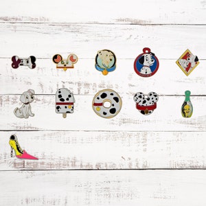 May include: A collection of 11 enamel pins featuring Dalmatian dogs, a donut, an ice cream cone, a shoe, and a bottle. The pins are colorful and have a cartoon style.