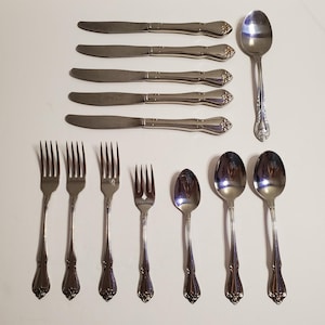 May include: A set of stainless steel cutlery, including knives, forks, and spoons. The silverware has decorative handles and a polished finish. The set includes multiple forks, spoons of different sizes, and knives.