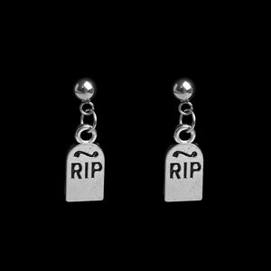 May include: A pair of silver-colored earrings. Each earring features a small, round stud connected to a chain, which leads to a tombstone charm. The tombstone charms have the letters "RIP" engraved on them. The background is black.