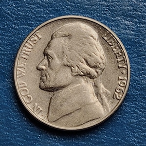 May include: A silver US nickel coin with the profile of Thomas Jefferson on the obverse. The coin reads "IN GOD WE TRUST" and "LIBERTY 1952".