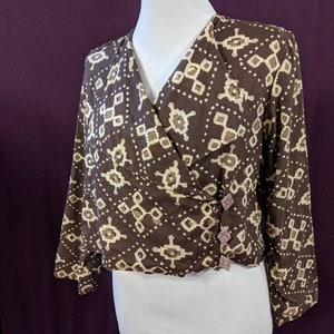 Puede incluir: Un top envolvente marrón con un estampado geométrico en beige y blanquecino. El top de manga larga presenta un cuello en V y se abrocha con tres botones decorativos. El top se exhibe en un maniquí blanco.