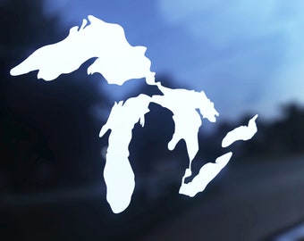 May include: A white decal of the Great Lakes region, including Superior, Michigan, Huron, Erie, and Ontario. The decal is a solid white shape against a blurred blue and black background.