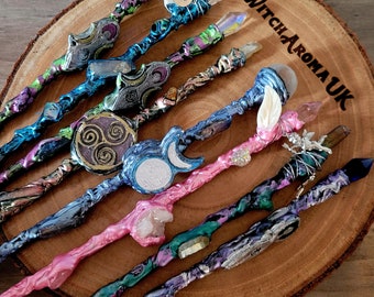 Puede incluir: Una colección de ocho varitas coloridas con diversos acentos de cristal y piedras preciosas. Las varitas se muestran sobre una superficie de madera con el texto "Witch Aroma UK" visible.
