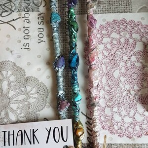 May include: Three colorful wands with crystals and wire wrapped around them. The wands are on a white surface with a pink and white doily. The wands are made with different colored stones and wire. The wands are about 10 inches long. The wands are handmade and unique. Thank you for supporting my small business! Your order means the world to me. Love your purchase please leave a review. Scent Sational@louisedale 1402 Scentsational 1402