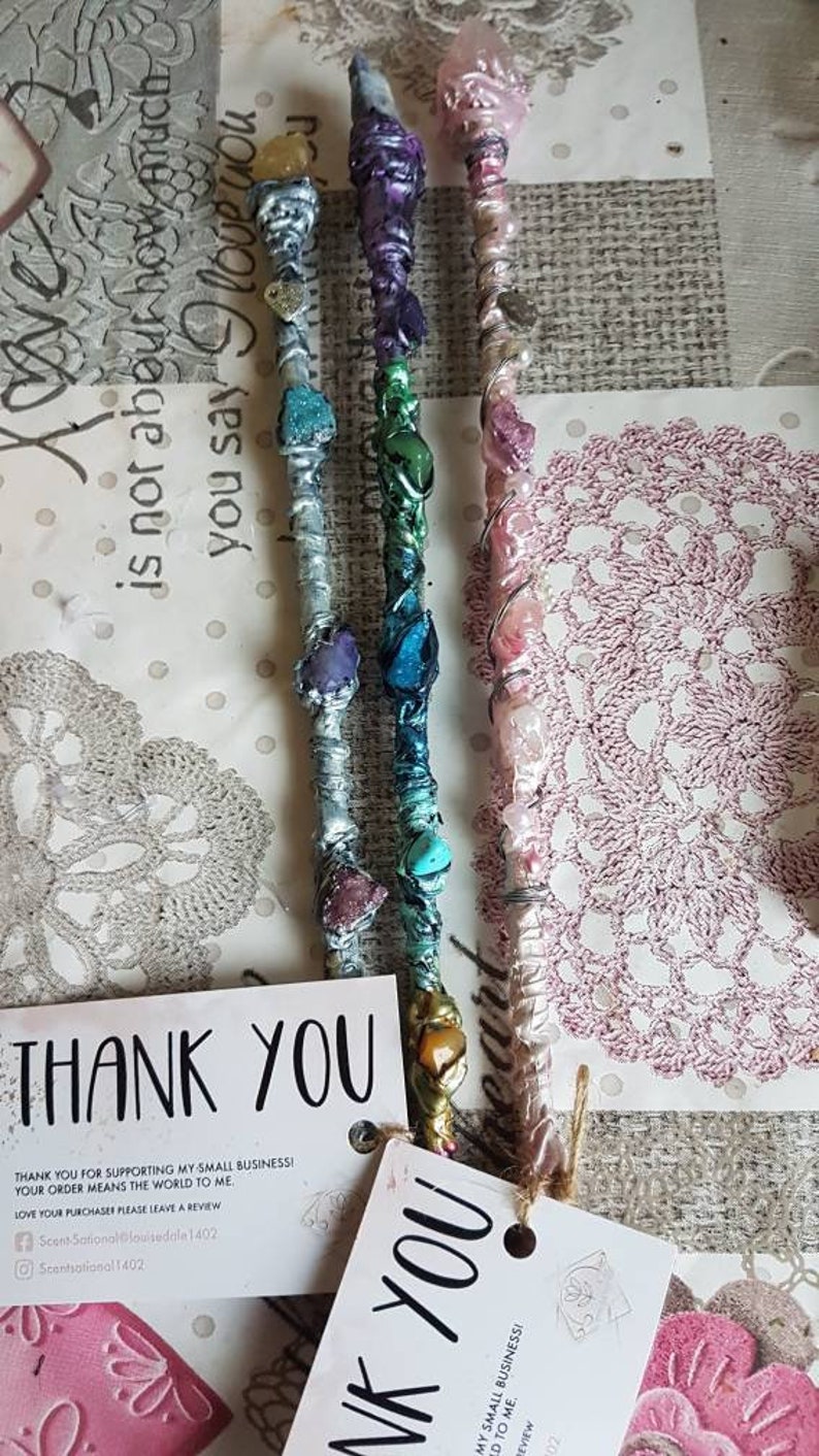 May include: Three colorful wands with crystals and wire wrapped around them. The wands are on a white surface with a pink and white doily. The wands are made with different colored stones and wire. The wands are about 10 inches long. The wands are handmade and unique. Thank you for supporting my small business! Your order means the world to me. Love your purchase please leave a review. Scent Sational@louisedale 1402 Scentsational 1402