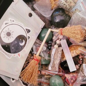 May include: A collection of various herbs, crystals, and other magical ingredients in a black container. The items are arranged in small plastic bags and include a small broom, a yin yang symbol sticker, and a green crystal. The bags are labeled with the names of the herbs, such as "Lavender" and "Sage".