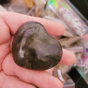 May include: A heart-shaped labradorite crystal with a dark gray and black color. The crystal is smooth and polished, with a slight sheen.