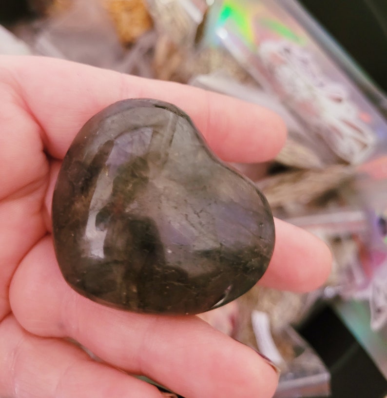 May include: A heart-shaped labradorite crystal with a dark gray and black color. The crystal is smooth and polished, with a slight sheen.