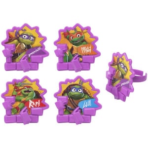 May include: A collection of Teenage Mutant Ninja Turtles rings. Each ring features a different turtle character emerging from a purple brick wall. The characters are set against a yellow burst background, with the character's name displayed.
