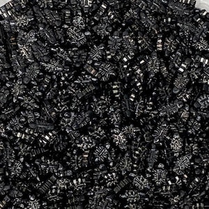 May include: A close-up image of a large quantity of black licorice candy shaped like snowflakes. The candy is shiny and has a slightly textured surface.