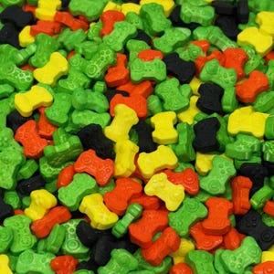 May include: A close-up shot of colorful candy shaped like video game controllers. The candy pieces are in various colors, including green, yellow, orange, and black. The candy is scattered, creating a vibrant and playful pattern.