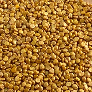 May include: A close-up image of gold-colored sprinkles. The sprinkles are small, round, and have a metallic sheen.