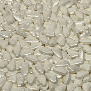 May include: A large quantity of white pearl-like cloud shaped sprinkles. The sprinkles are small and have a slightly iridescent sheen.