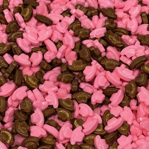 May include: A close-up shot of a pile of pink and brown cowboy hat-shaped sprinkles. The sprinkles are scattered, with the pink hats appearing to be a lighter shade than the brown ones. The image is well-lit, showing the details of the sprinkles.