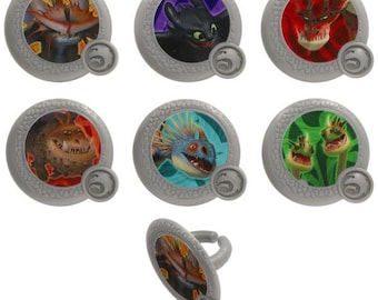 May include: A collection of gray plastic rings featuring colorful images of dragons. Each ring has a circular design with a dragon image in the center. The rings are designed with a textured border and a small dragon emblem.