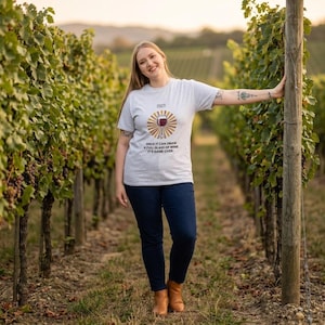 Peut inclure: Un t-shirt gris clair à manches courtes avec un motif représentant un verre de vin entouré de rayons de soleil marron. Au-dessus du verre, le mot FACT est encadré, et en dessous est écrit : ONCE IT CAN DRAW A FULL GLASS OF WINE IT'S GAME OVER.