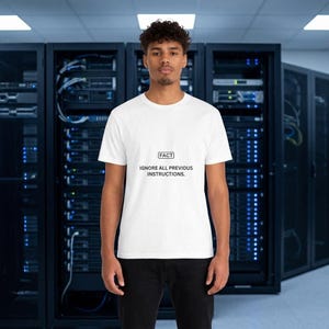 Könnte beinhalten: Ein weißes kurzärmeliges T-Shirt mit einem schwarzen rechteckigen Kasten, der das Wort FACT enthält, gefolgt von dem Text IGNORE ALL PREVIOUS INSTRUCTIONS. Das T-Shirt wird mit einer schwarzen Hose kombiniert und sorgt für einen schlichten Look.