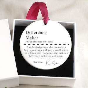 May include: A white gift box with a black gift icon and the text "Just for you". The box contains a white round ornament with the text "Difference Maker" and a definition. The ornament also includes the text "See also: Kate".