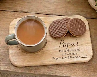 May include: A rectangular wooden serving board featuring a circular indentation for a mug and space for snacks. The board is engraved with the text: Papa's tea and biscuits, Lots of love, Poppy, Lily & Freddie XXX. A mug of tea and two chocolate biscuits are placed on the board.
