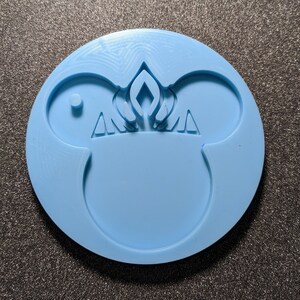 May include: A light blue silicone mold shaped like a cartoon mouse head with a crown on top. The mold is designed for making resin crafts.